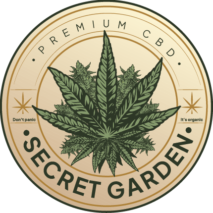 The image shows a circular logo for "Secret Garden." The logo features a detailed, symmetrical design with a large cannabis leaf in the center, surrounded by smaller leaf motifs and decorative elements. The main colors are green for the leaves and a light tan for the background. The text "Secret Garden" is integrated at the bottom of the circle in a stylized, serif font. There are also ornamental swirls that fill the background space within the circle. The overall style is rustic with a naturalistic feel.